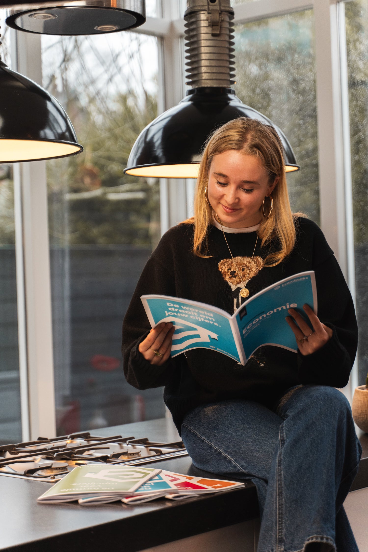 Student zit ontspannen op een keukenblad en leest een ExamBooks-economieboek, terwijl ze zich voorbereidt op haar eindexamens.