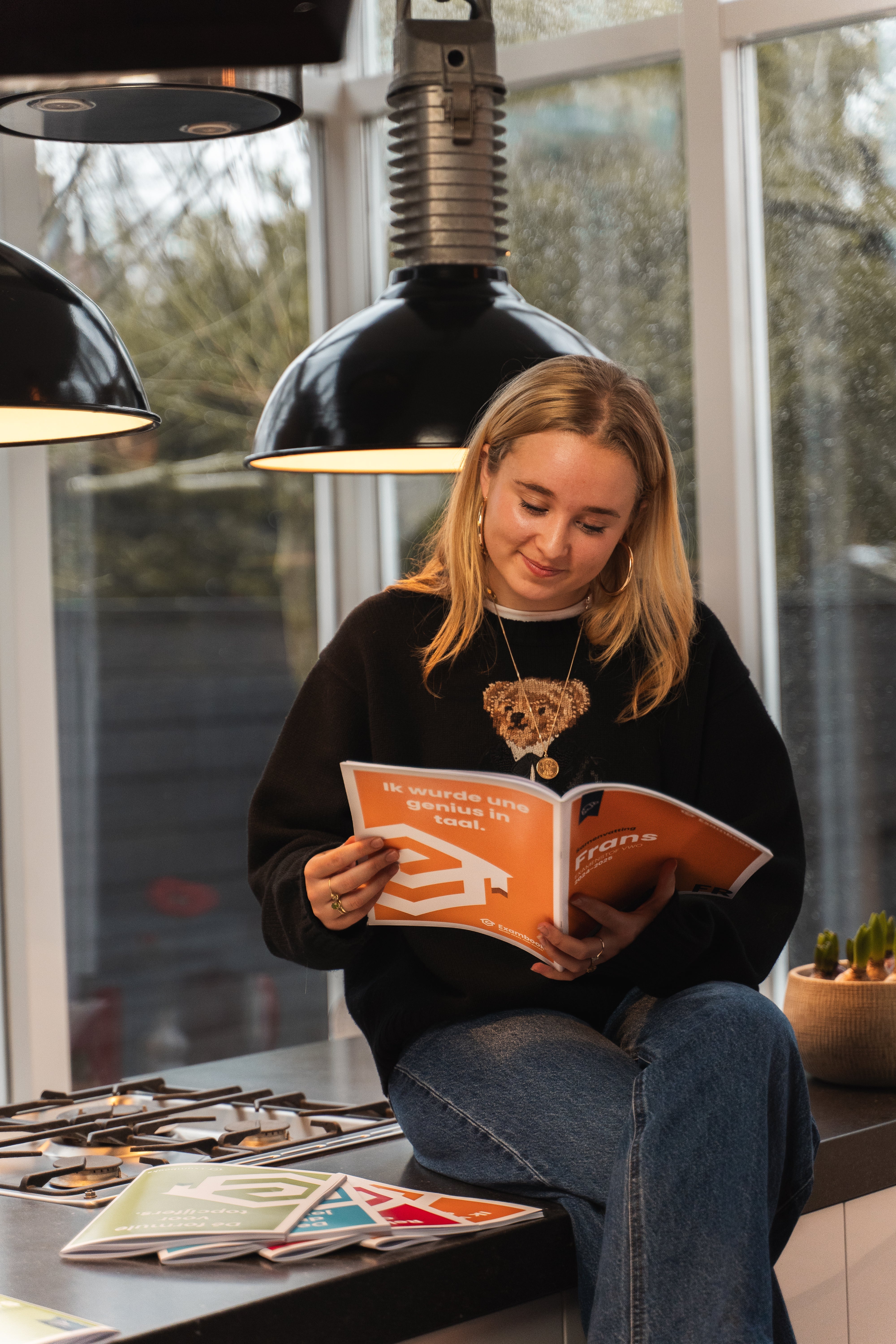 Student zit ontspannen op een keukenblad en leest een ExamBooks-economieboek, terwijl ze zich voorbereidt op haar eindexamens.