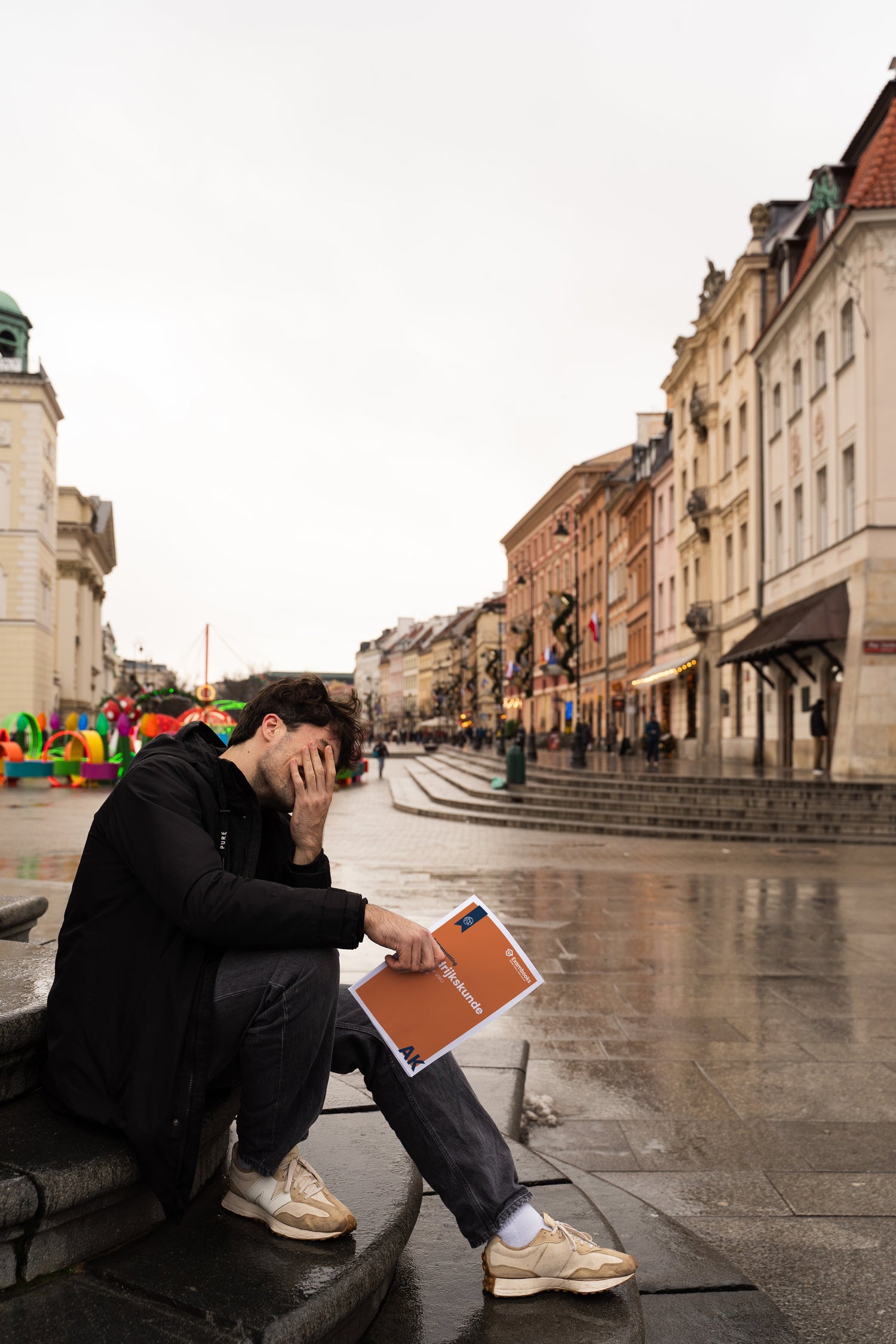 Student zit op een stenen trap in een Europese stad, verdiept in gedachten met een ExamBooks-studieboek in de hand, terwijl hij zich voorbereidt op zijn eindexamens.