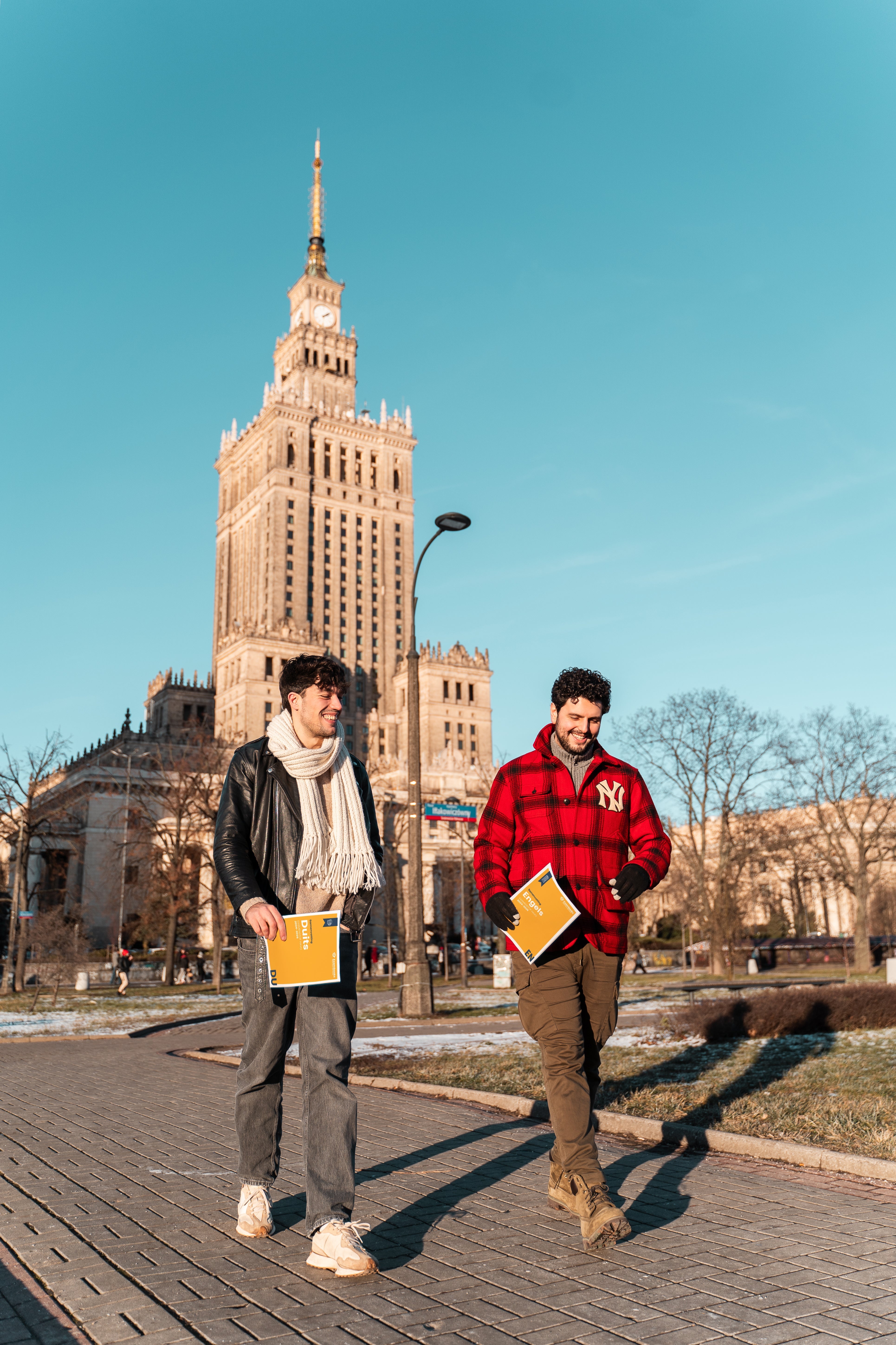 Twee studenten wandelen door een stadspark met ExamBooks-studieboeken in de hand, terwijl ze samen hun eindexamenvoorbereiding bespreken.