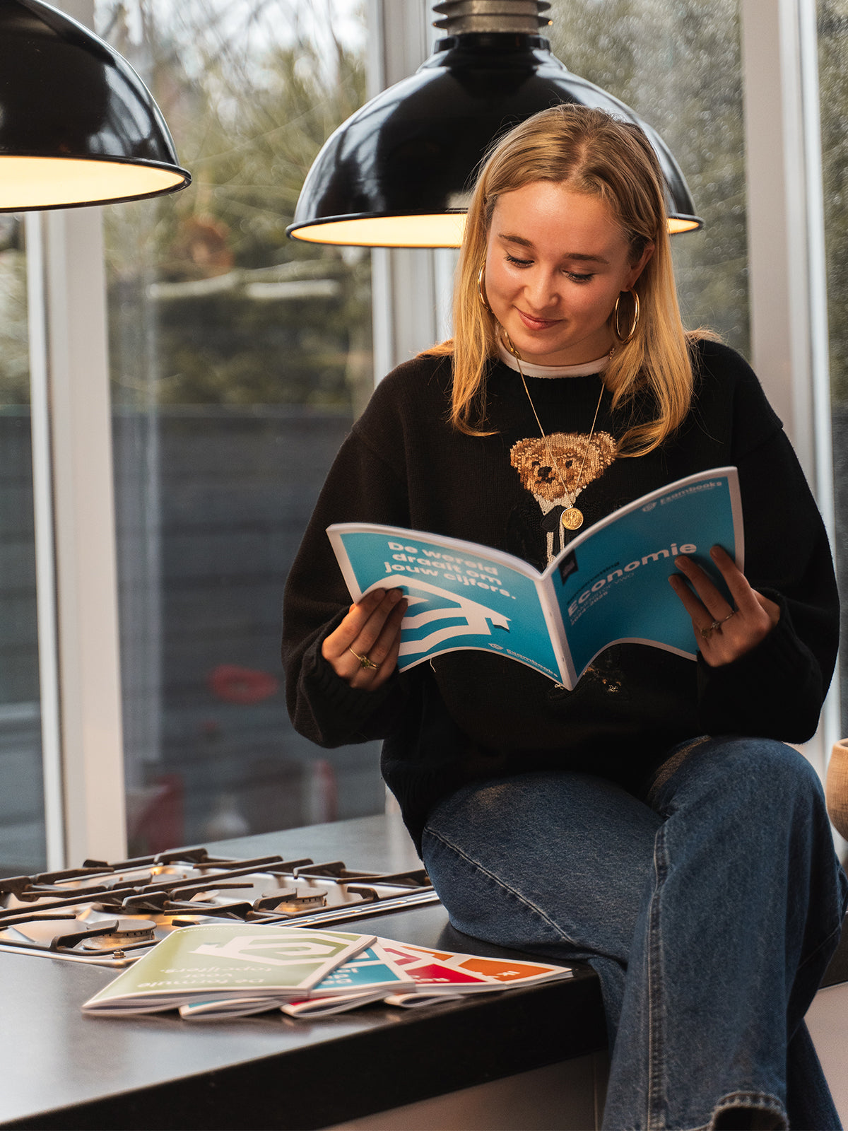 Student leest ontspannen een economieboek, met ExamBooks-studieboeken op tafel, als voorbereiding op haar eindexamens.