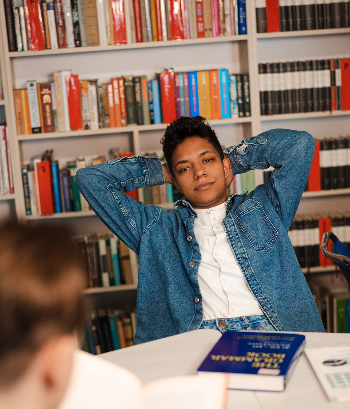 Student leunt ontspannen achterover in een bibliotheek, omringd door boeken, na een effectieve studiesessie met ExamBooks ter voorbereiding op de eindexamens.